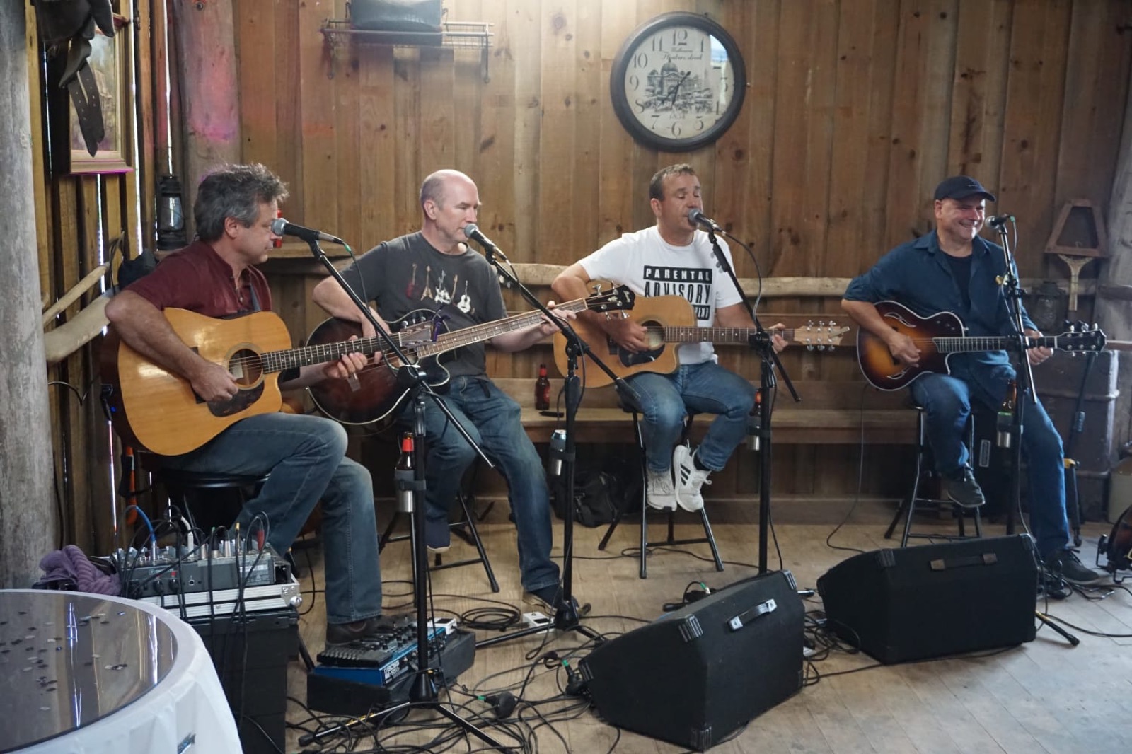 The four Barstools playing acoustic guitars on stools in a timber barn